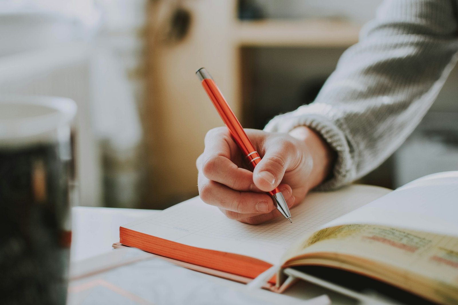 A hand writing notes in a notebook with a red pen