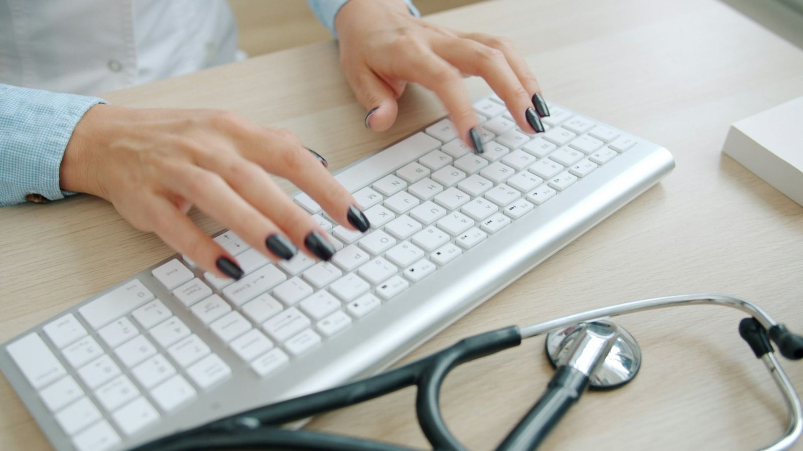 A doctor typing at a keyboard with a stethoscope on the desk
