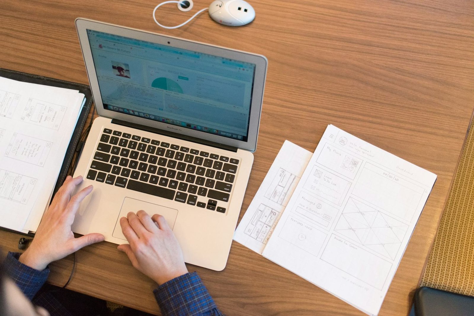 Hands on a laptop beside printed notes on a wooden desk
