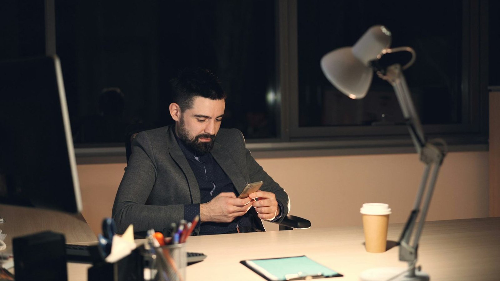 A man checking his phone at a desk late in the evening